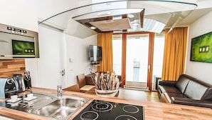 A modern kitchen with a built-in stove, a sink, and a coffee maker. There is a dining area with a table and chairs, and a living room with a sofa. - Apartment Emma by Interhome (Kaprun)