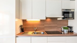 A modern kitchen with white cabinets, a stainless steel sink, a built-in oven, and a wooden backsplash. - Apartment Emma by Interhome (Kaprun)