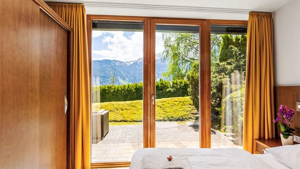 A bedroom with a bed, a view of a landscaped garden, and a sliding glass door leading to an outdoor area. - Apartment Emma by Interhome (Kaprun)