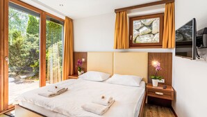 A modern bedroom with a large bed, wooden headboard, and a view of a forest through floor-to-ceiling windows. - Apartment Emma by Interhome (Kaprun)