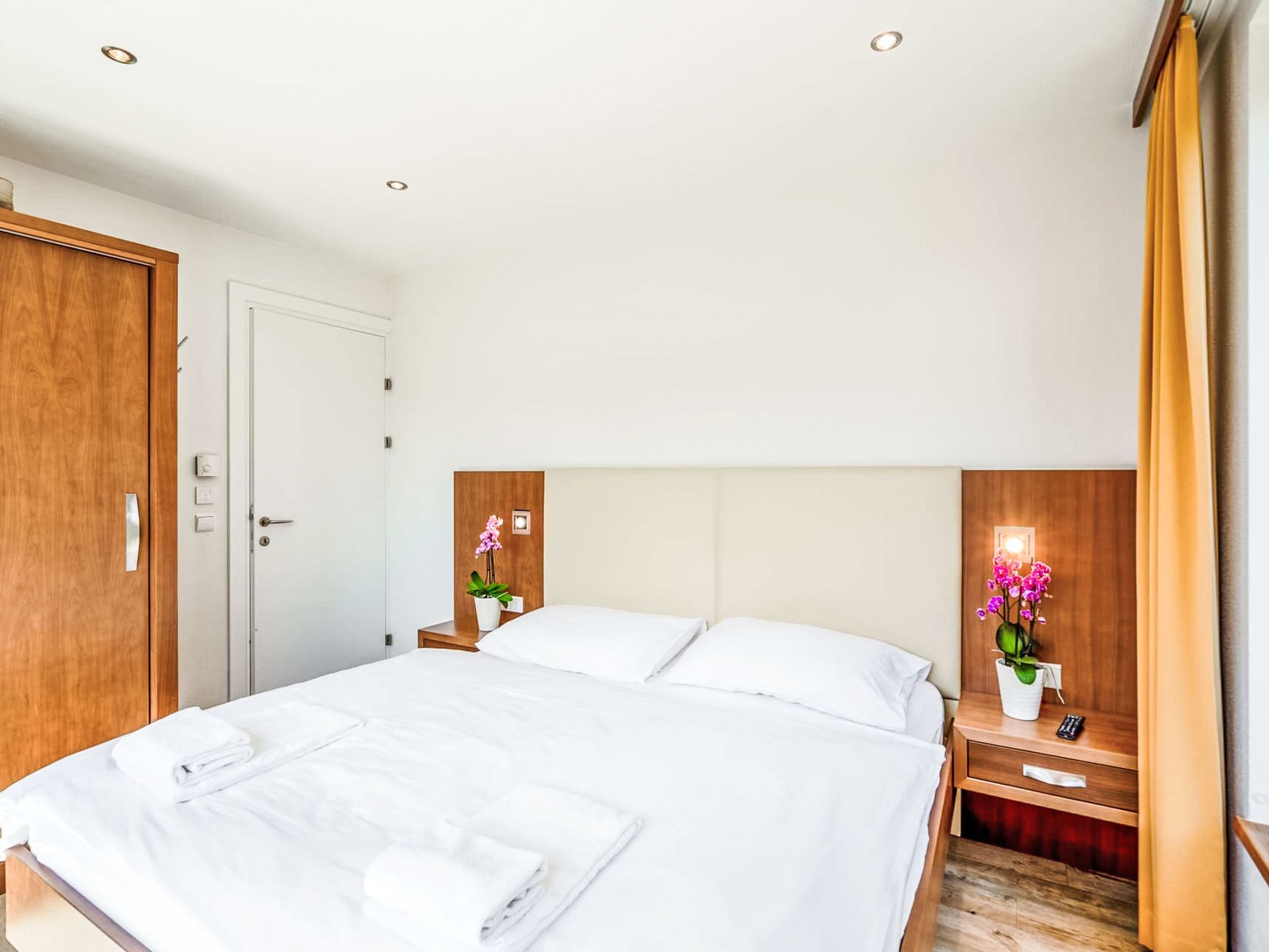 Een hotelkamer met een groot bed, houten hoofdeinde, nachtkastjes met lampen en een deur.