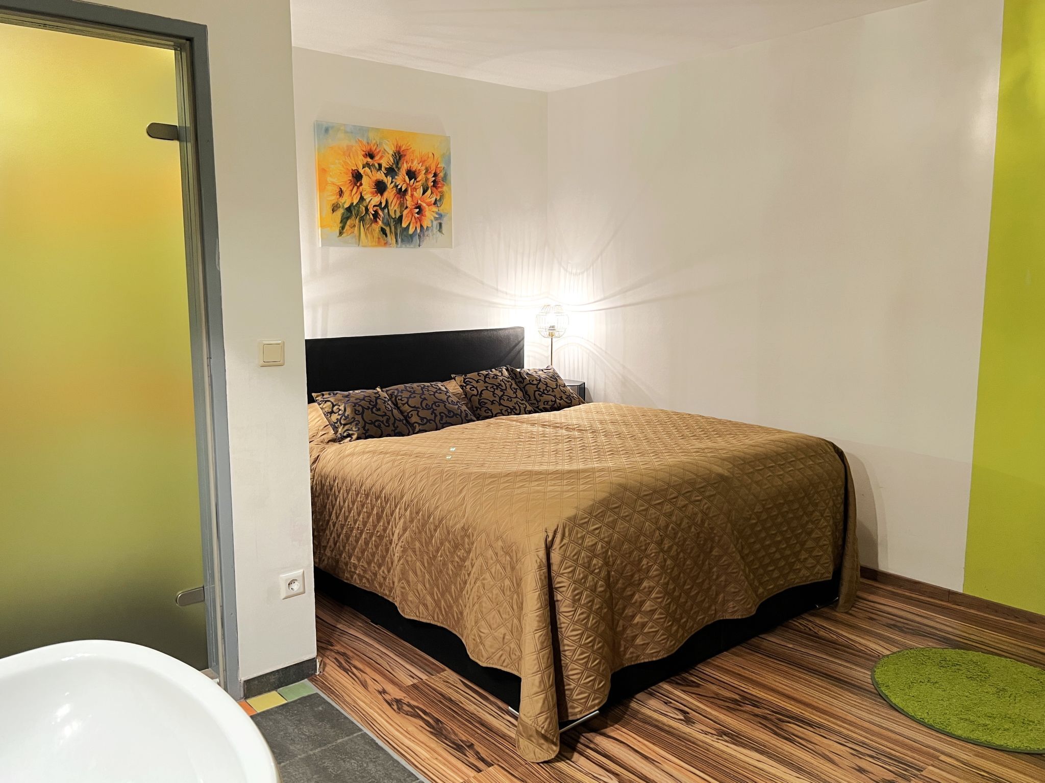 A bedroom with a bed, a painting, a bedside lamp, and a green rug.