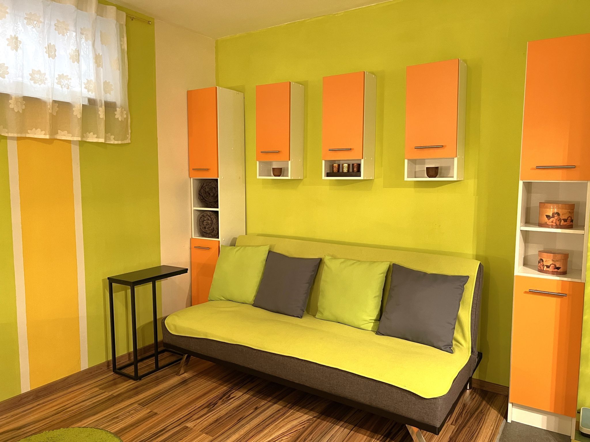 A room with a sofa, wooden flooring, and orange cabinets.