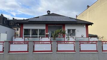 Punavalkoinen, kaksikerroksinen talo, jossa on tiilikatto ja pieni kuisti, jota koristavat erilaiset koriste-esineet.