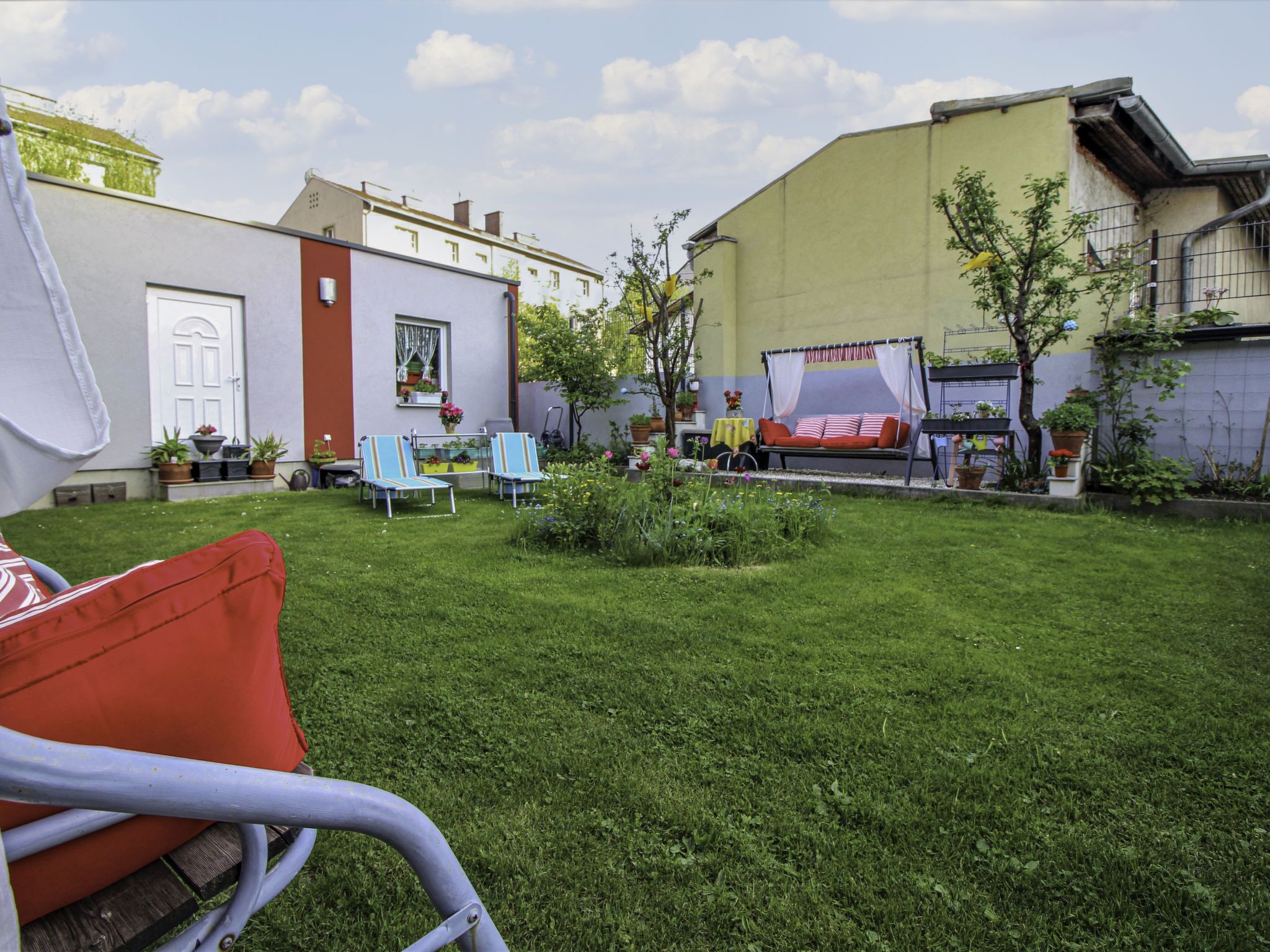 A well-maintained backyard with a lawn, two lounge chairs, a small garden, and a patio area with a table and chairs.