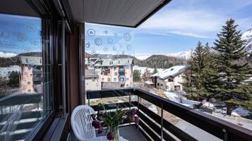 Un balcon avec une table et des chaises, un vase rempli de fleurs et une vue sur des bâtiments et des montagnes.