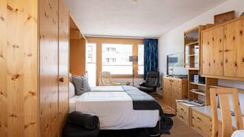 Ein Hotelzimmer mit einem großen Bett, einem Holzschrank, einem Schreibtisch mit Stuhl, einem Fernseher und einem Fenster mit Vorhängen.