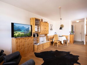 Un salon moderne doté d’un téléviseur à écran plat, de meubles en bois, d’un coin repas et d’un tapis en cuir noir.