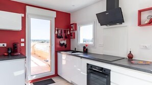 A modern kitchen with white cabinets, a black countertop, and a red accent wall. - Les Roches Bleues by Interhome (Le Pradet)