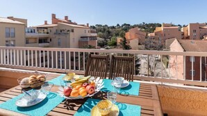 A balcony with a table set for breakfast, featuring fruits and pastries, overlooking a residential area with similar buildings. - Les Roches Bleues by Interhome (Le Pradet)