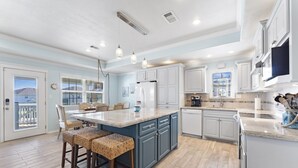Una cocina amplia con una isla grande, armarios blancos y vistas al exterior.