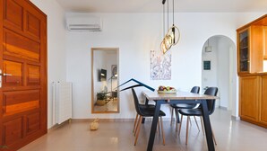 Uma sala de jantar com porta de madeira, paredes brancas, mesa de jantar com cadeiras e luminária pendente.