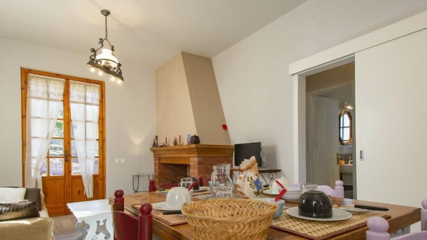 Un salon chaleureux avec une cheminée, un coin repas avec une grande table et une cuisine équipée d’un téléviseur.