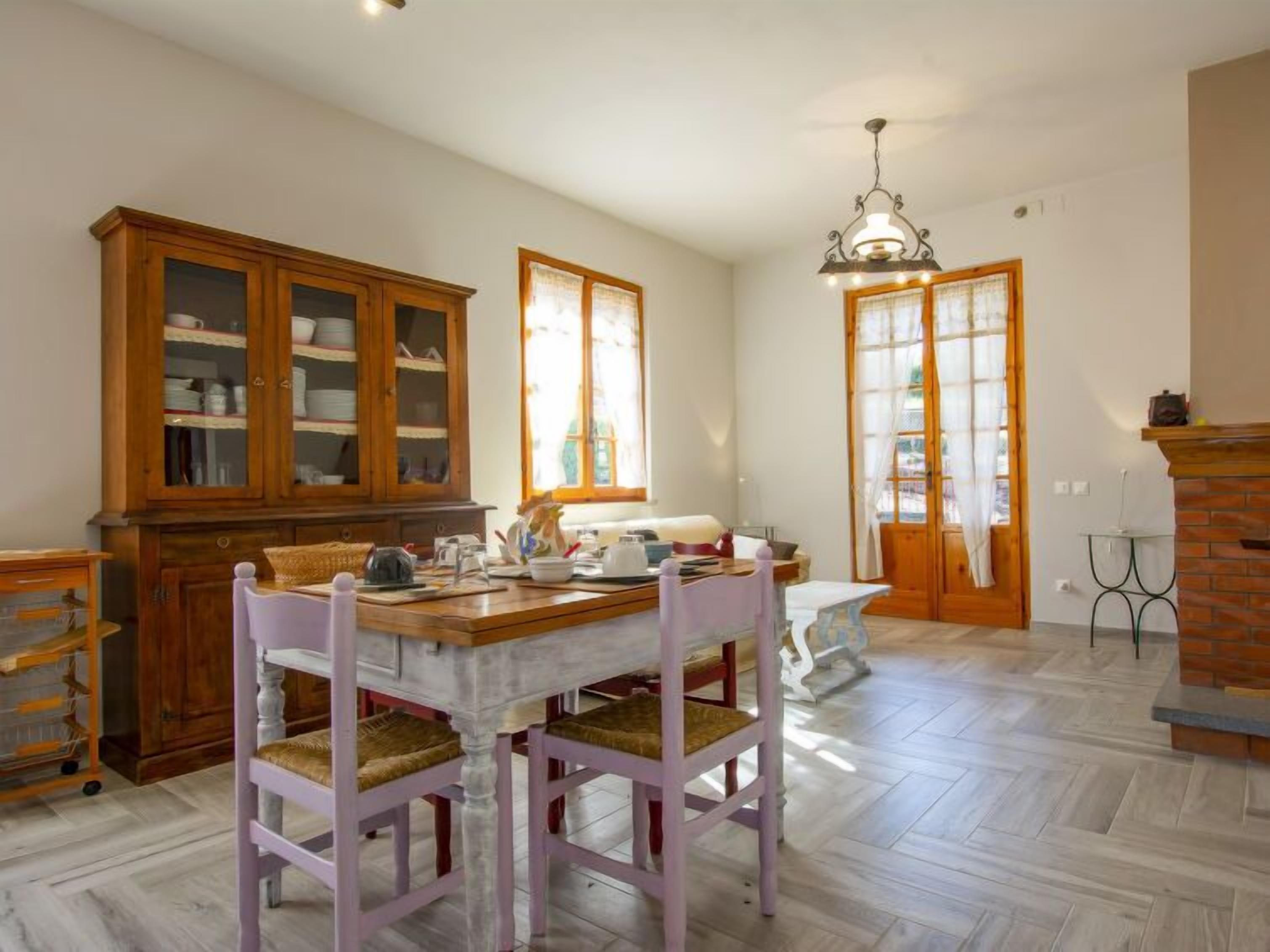 A spacious kitchen with a wooden cabinet, a dining table with chairs, and a hanging light fixture.
