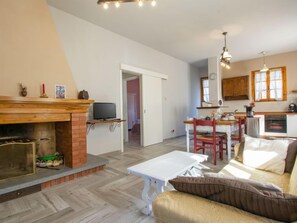 Ein gemütliches Wohnzimmer mit Kamin, eine Essecke mit Tisch und Stühlen sowie eine Küche mit Schränken und einem Fenster.
