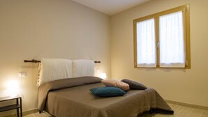 Une chambre à coucher avec un lit, une table de chevet, une fenêtre avec des rideaux et un tapis coloré.