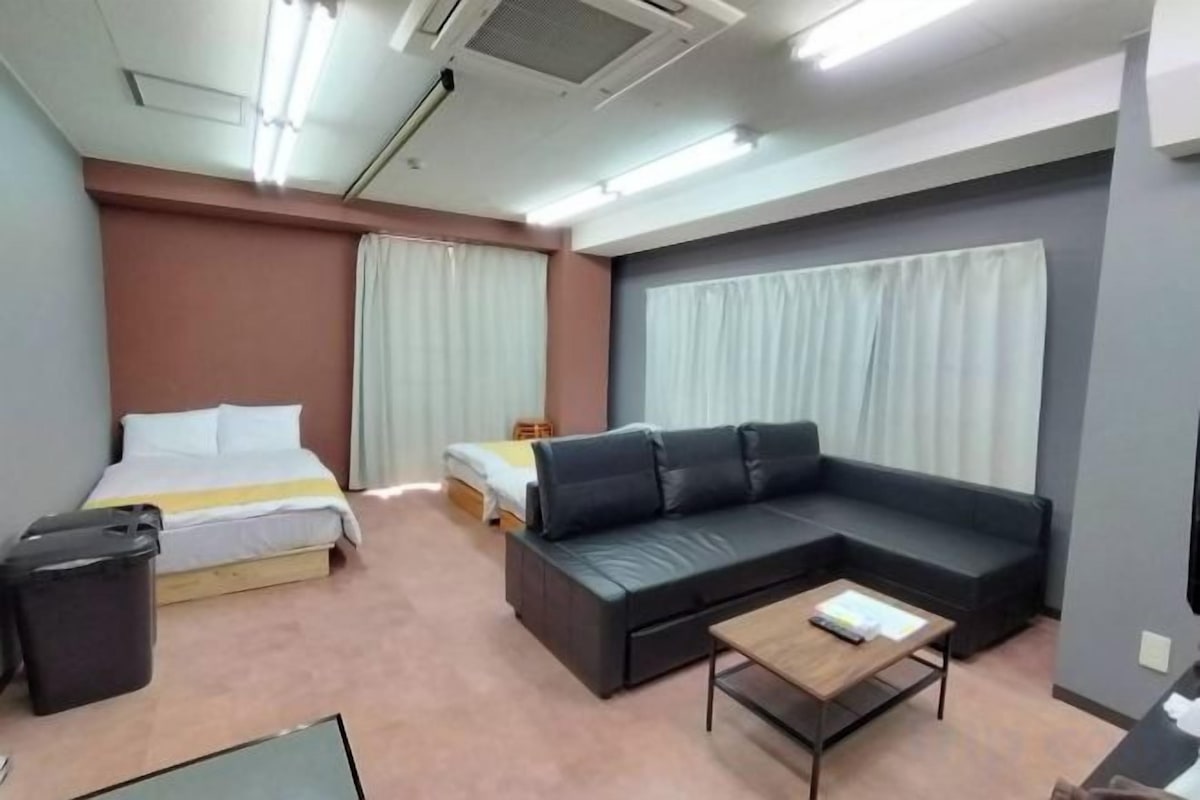 Una habitación de hotel con cama, sofá, mesa de centro y un cubo de basura.