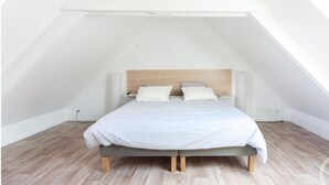 A bedroom with a sloped ceiling, a bed with a wooden headboard, and light-colored wooden flooring.