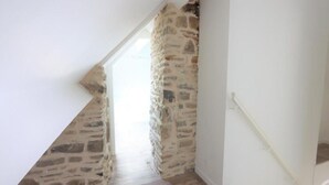 A narrow stairway with a stone wall on one side and a white wall on the other, leading to a bright room.