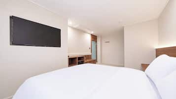 A hotel room with a bed, a TV mounted on the wall, a wooden nightstand, and a door with a handle.