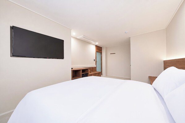 A hotel room with a bed, a TV mounted on the wall, a wooden nightstand, and a door with a handle.
