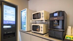 A vending machine with a digital display, a microwave, and a coffee machine on a counter. - CentroStay (Incheon)
