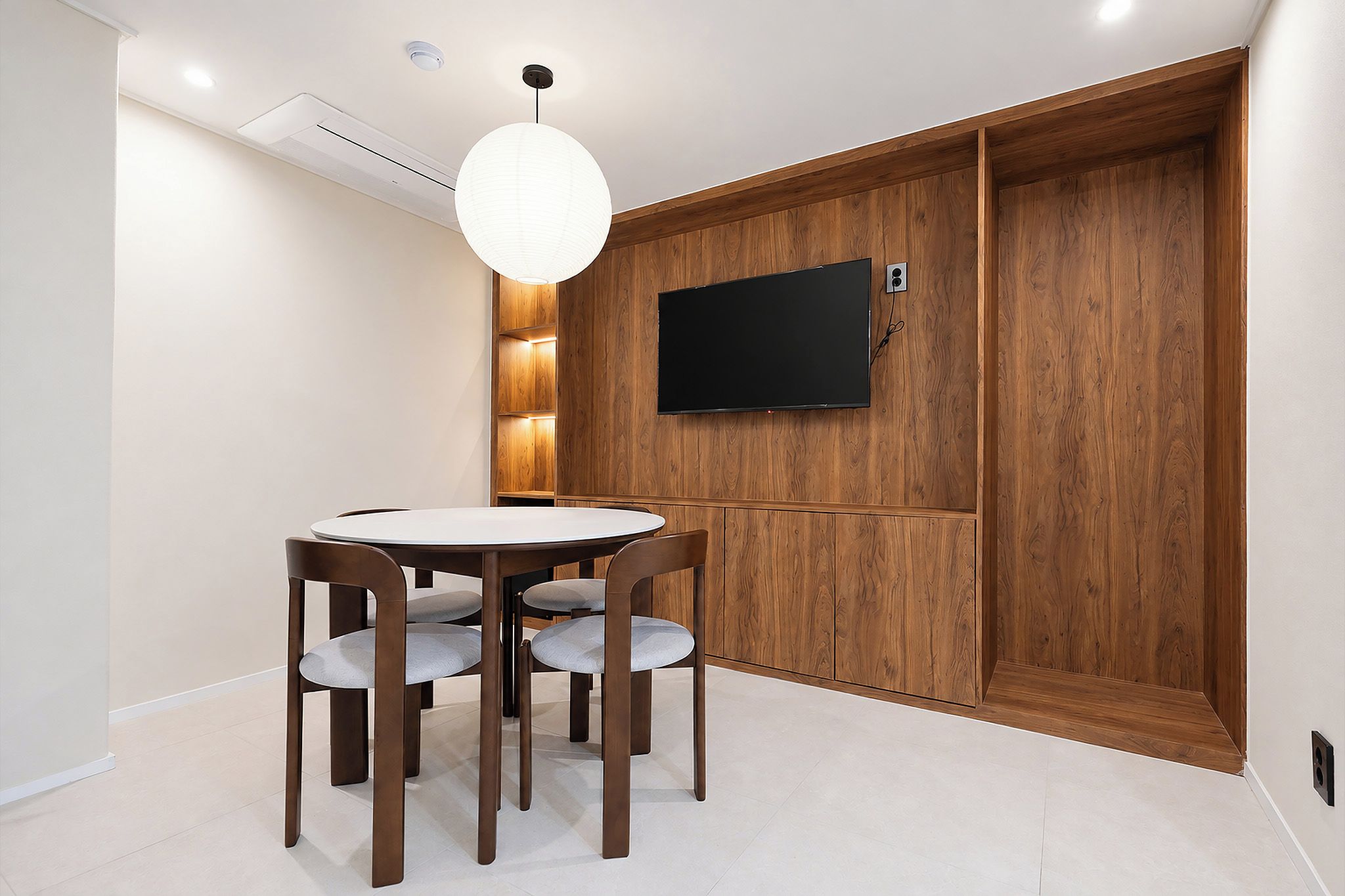 A dining area with a round table and four chairs, a wall-mounted television, and a wooden panel wall.