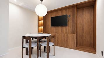 A dining area with a round table and four chairs, a wall-mounted television, and a wooden panel wall.