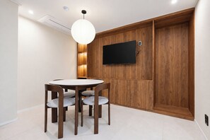 Un comedor con una mesa redonda y cuatro sillas, un televisor montado en la pared y un revestimiento de panel de madera.