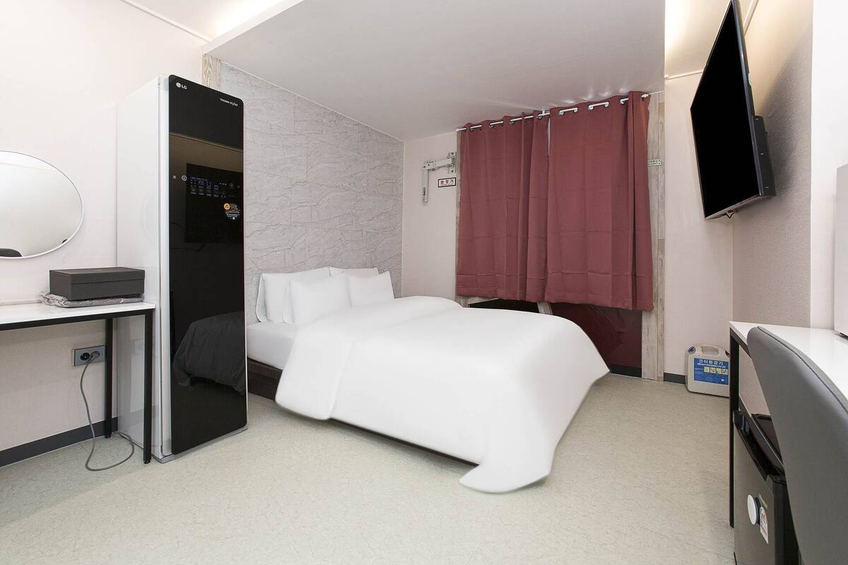A hotel room with a bed, a desk with a computer, a TV, and a bathroom with a shower curtain.