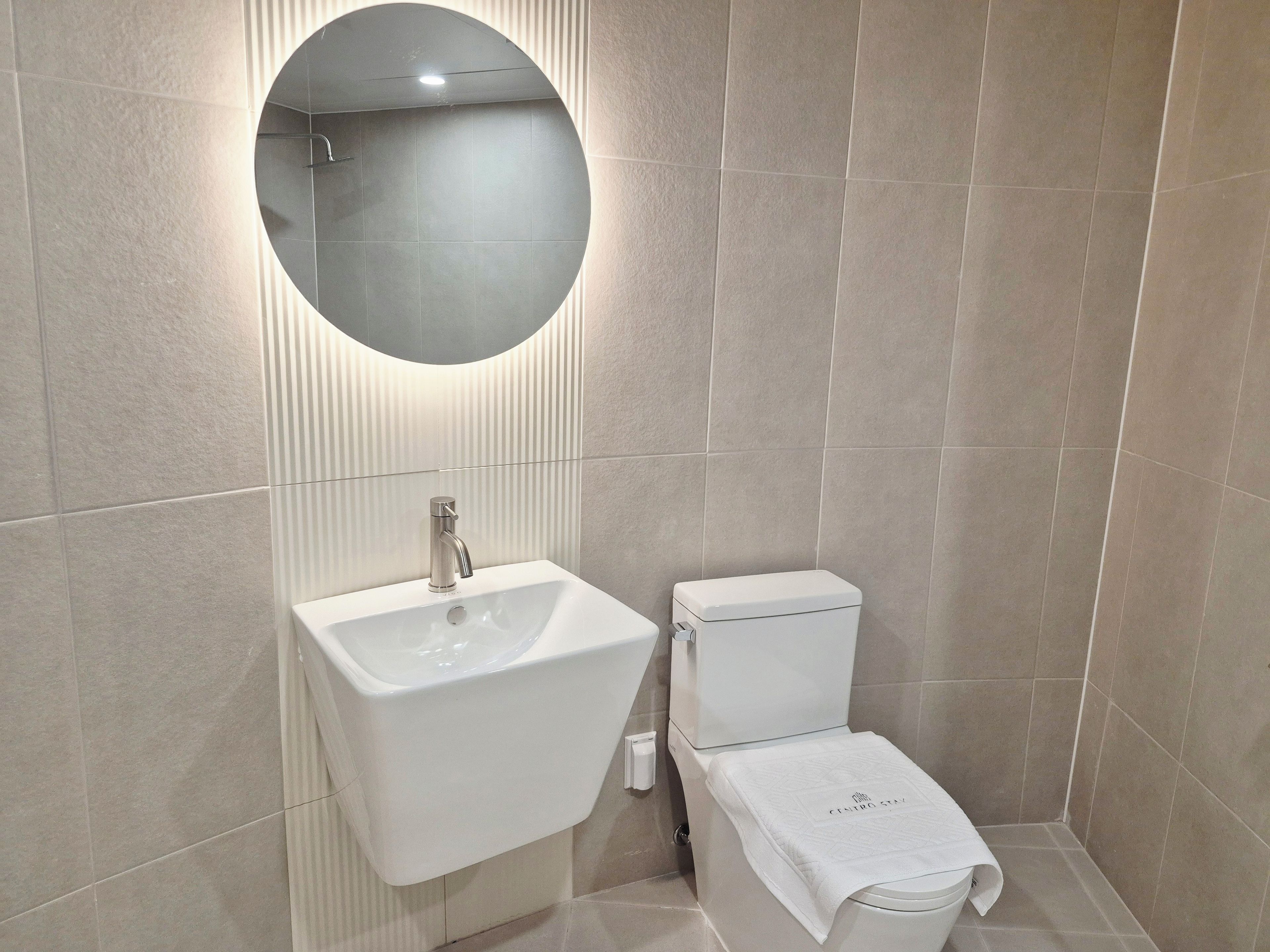 Un baño con un lavamanos blanco, un inodoro y un espejo redondo.