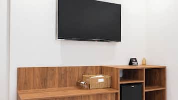 A room with a flat-screen TV mounted on the wall, a wooden bench with storage baskets, and a black appliance.