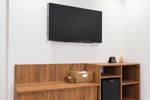 Una habitación con un televisor de pantalla plana montado en la pared, un banco de madera con cestas de almacenamiento y un electrodoméstico negro.