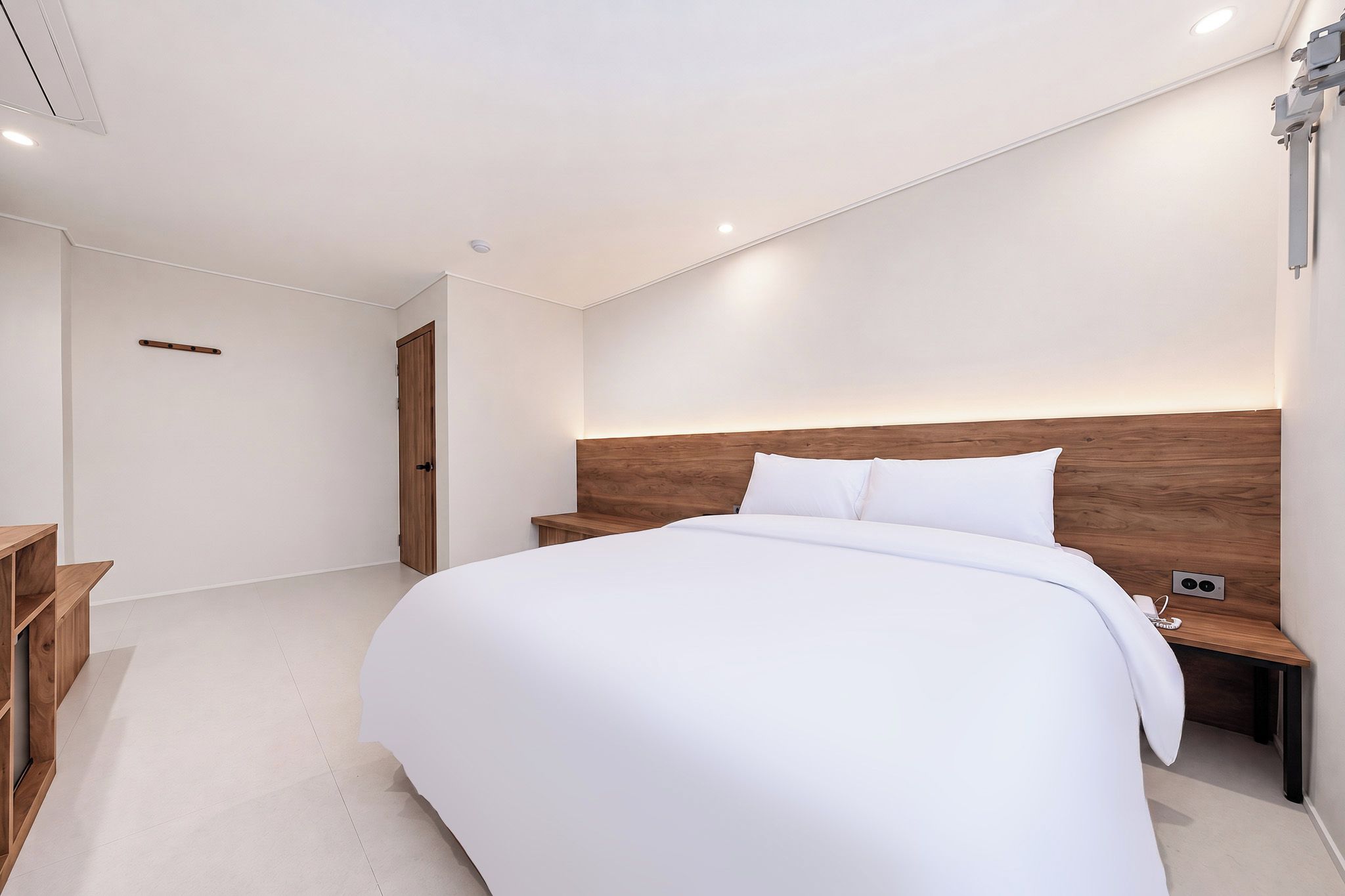 A modern bedroom with a large bed, wooden headboard, bedside tables, and a built-in shelf.