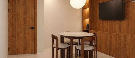 A dining area with a round table and four chairs, a wooden door, and a flat-screen TV mounted on the wall.