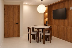 A dining area with a round table and four chairs, a wooden door, and a flat-screen TV mounted on the wall. - CentroStay (Incheon)