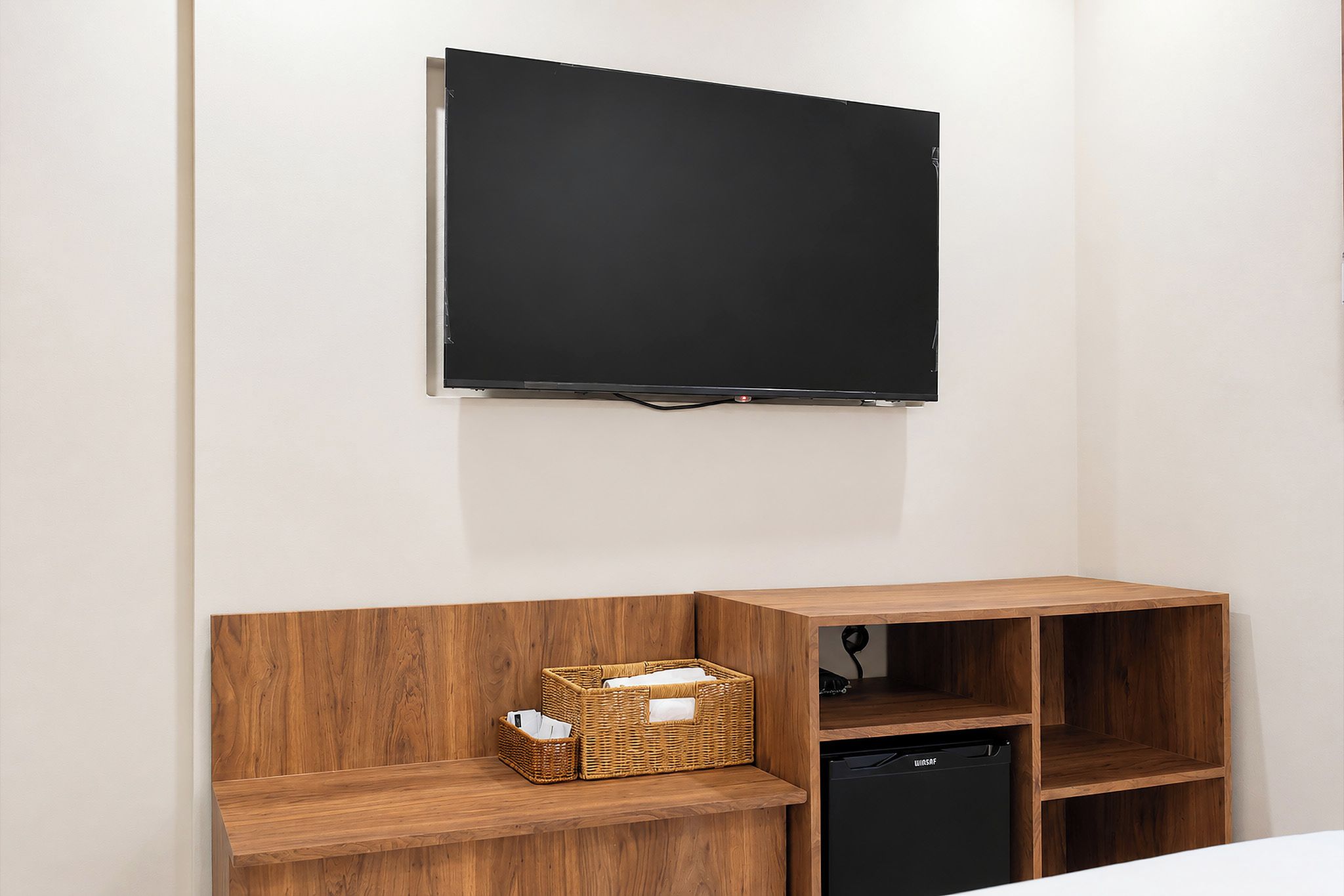A room with a mounted flat-screen TV, wooden shelving unit, and a black appliance.