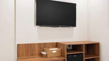 A room with a mounted flat-screen TV, wooden shelving unit, and a black appliance.