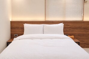 A neatly made bed with white bedding, a wooden headboard, and a bedside table with a lamp. - CentroStay (Incheon)