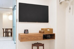 Ett modernt rum med en platt-TV som är monterad på väggen, en trähylla med en korg och en skylt samt en matplats med stolar och ett bord.