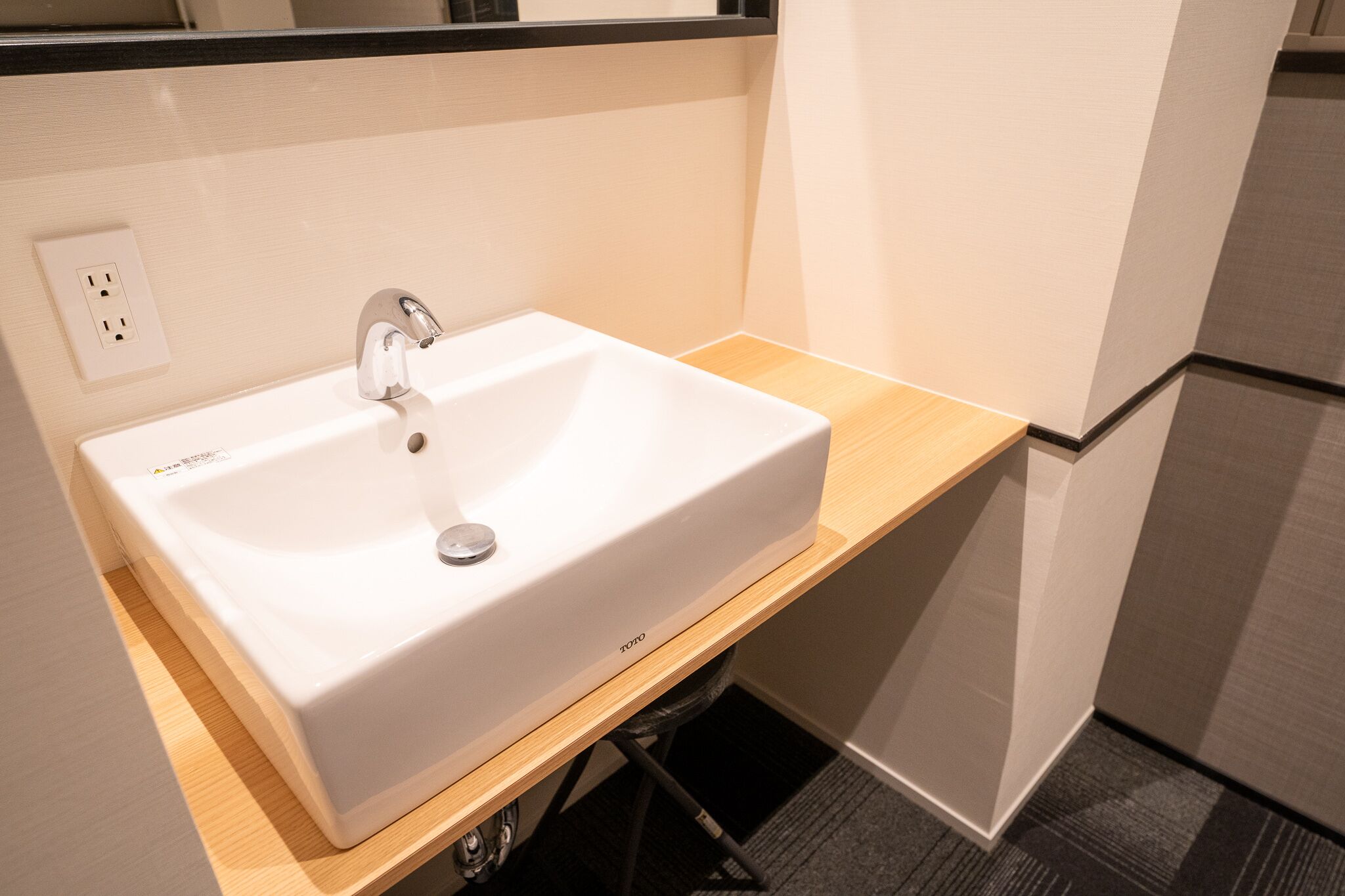 A white bathroom sink with a modern faucet, a wooden countertop, and a visible electrical outlet.