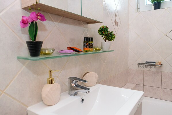 A bathroom with a white sink, a chrome faucet, a glass shelf with potted plants, and a shower area.