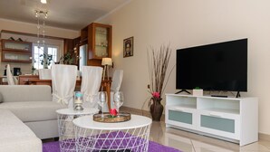 Un salon moderne avec un canapé, deux tables rondes ornées de bougies, un téléviseur à écran plat et un meuble blanc.