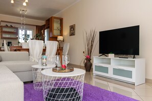 A modern living room with a sofa, two round tables with candles, a flat-screen TV, and a white cabinet.