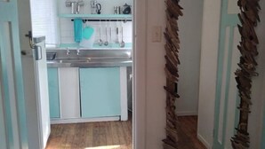A narrow hallway leading to a kitchen with a sink, cabinets, and a blue countertop. - BACH on BEACH- Pipi Palace. (Papamoa)