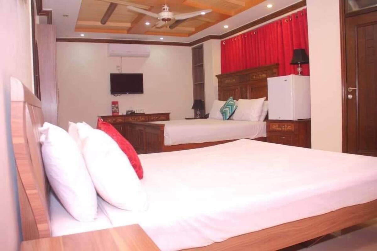 A bedroom with two beds, wooden headboards, a ceiling fan, a TV, and a red curtain.