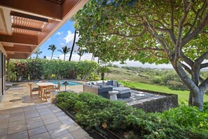 A patio with a pool, outdoor seating, and lush greenery.