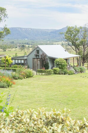 A rustic barn-style house with a large porch, surrounded by lush greenery and a well-maintained lawn.