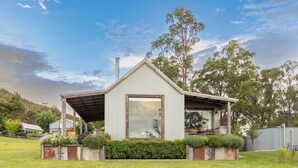 Une maison moderne dotée d’une grande fenêtre, d’un porche abrité et d’un jardin bien entretenu.