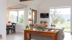 Un salon spacieux avec un plafond haut, une table à manger en bois, un canapé et une grande fenêtre donnant sur l’extérieur.